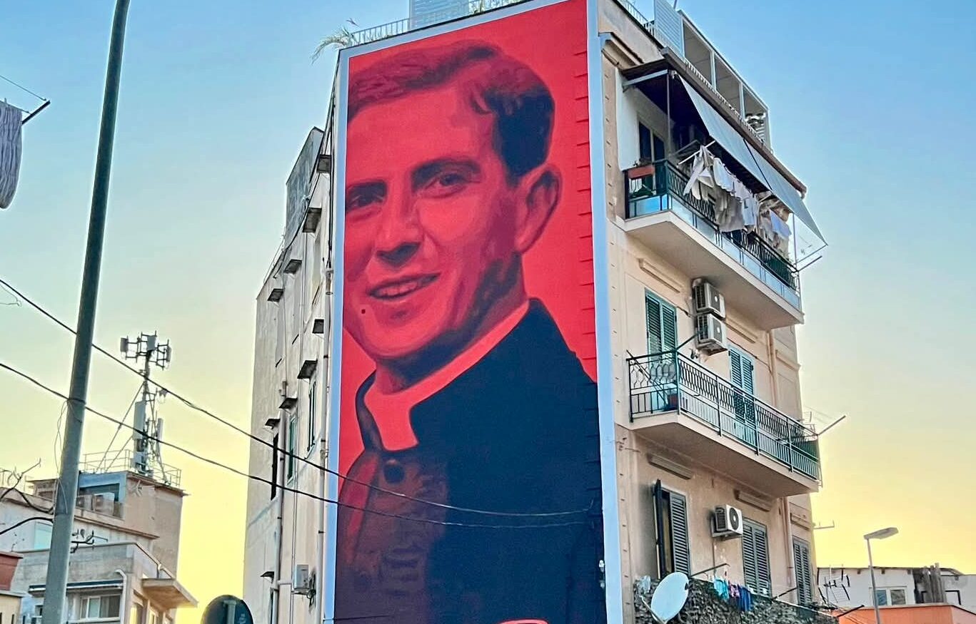 “Rosso assoluto”, il sorriso di un giovane Don Puglisi accende Brancaccio: tra bellezza e libertà il murale dell’artista Andrea Buglisi